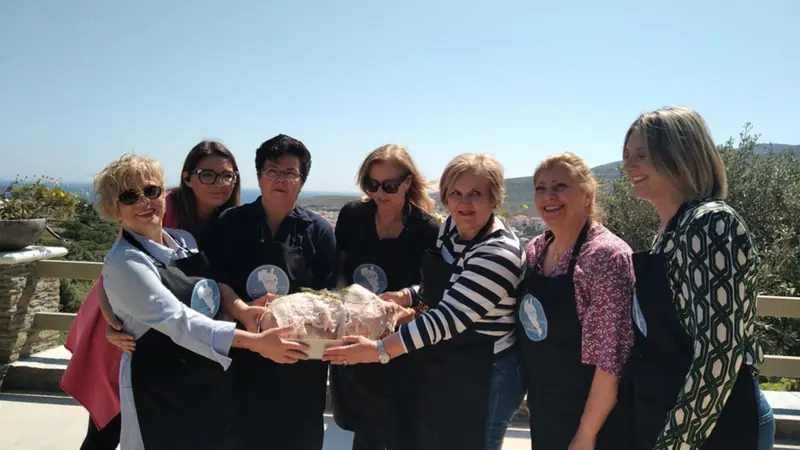 Μέλη του Συλλόγου κρατούν μαζί ένα καρβέλι ψωμί σε βεράντα με θέα
