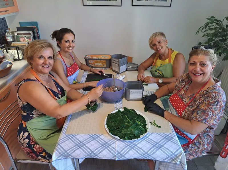 Γυναίκες καθαρίζουν χόρτα γύρω από τραπέζι με καρό τραπεζομάντιλο