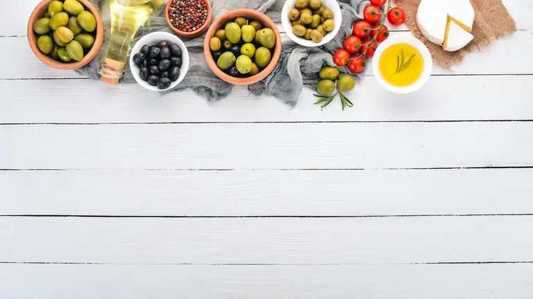 Ελιές, τυριά, ντομάτες και ελαιόλαδο σε μπολ πάνω σε λευκό ξύλινο τραπέζι